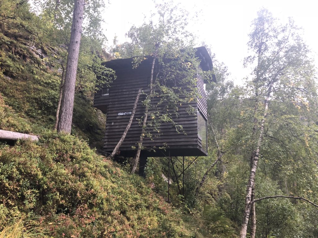 A small wooden cabin perched on a steep forested hillside